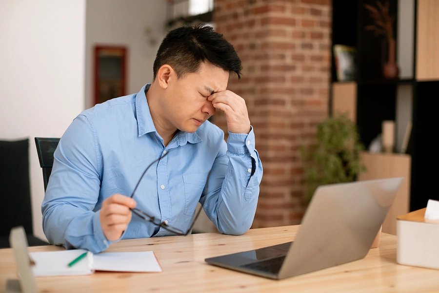 Tired male veteran holding his glasses and closing his eyes while working from home because he slept poorly due to sleep apnea 