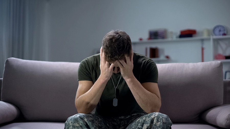 Young military man sits on a couch looking frustrated because his unaccredited VA coach exploited him